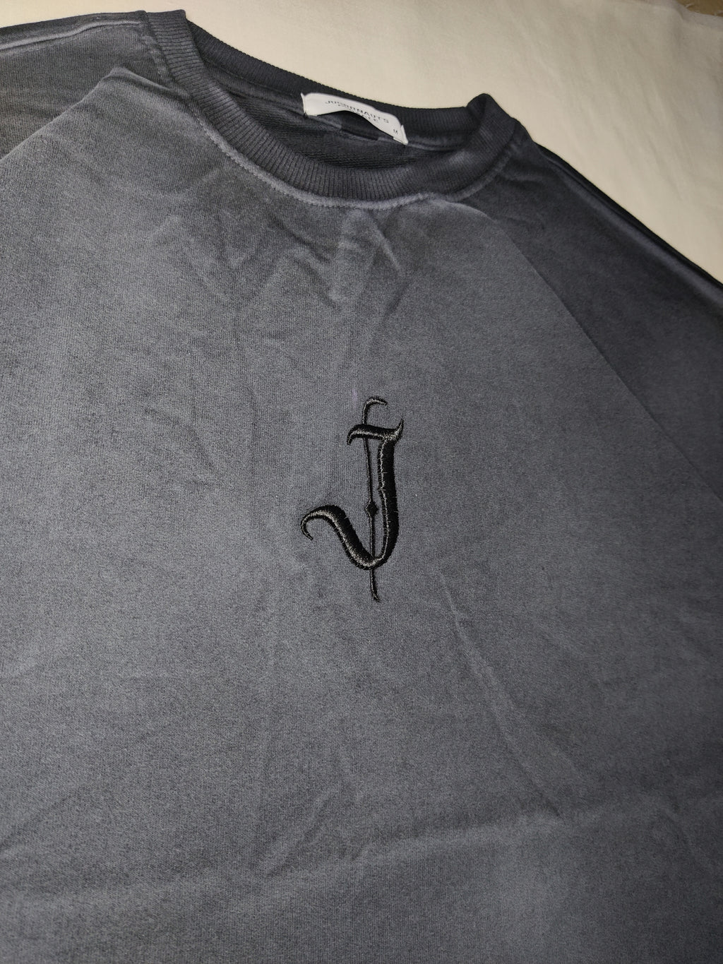 Gray tank top with a black embroidered design on a beige surface