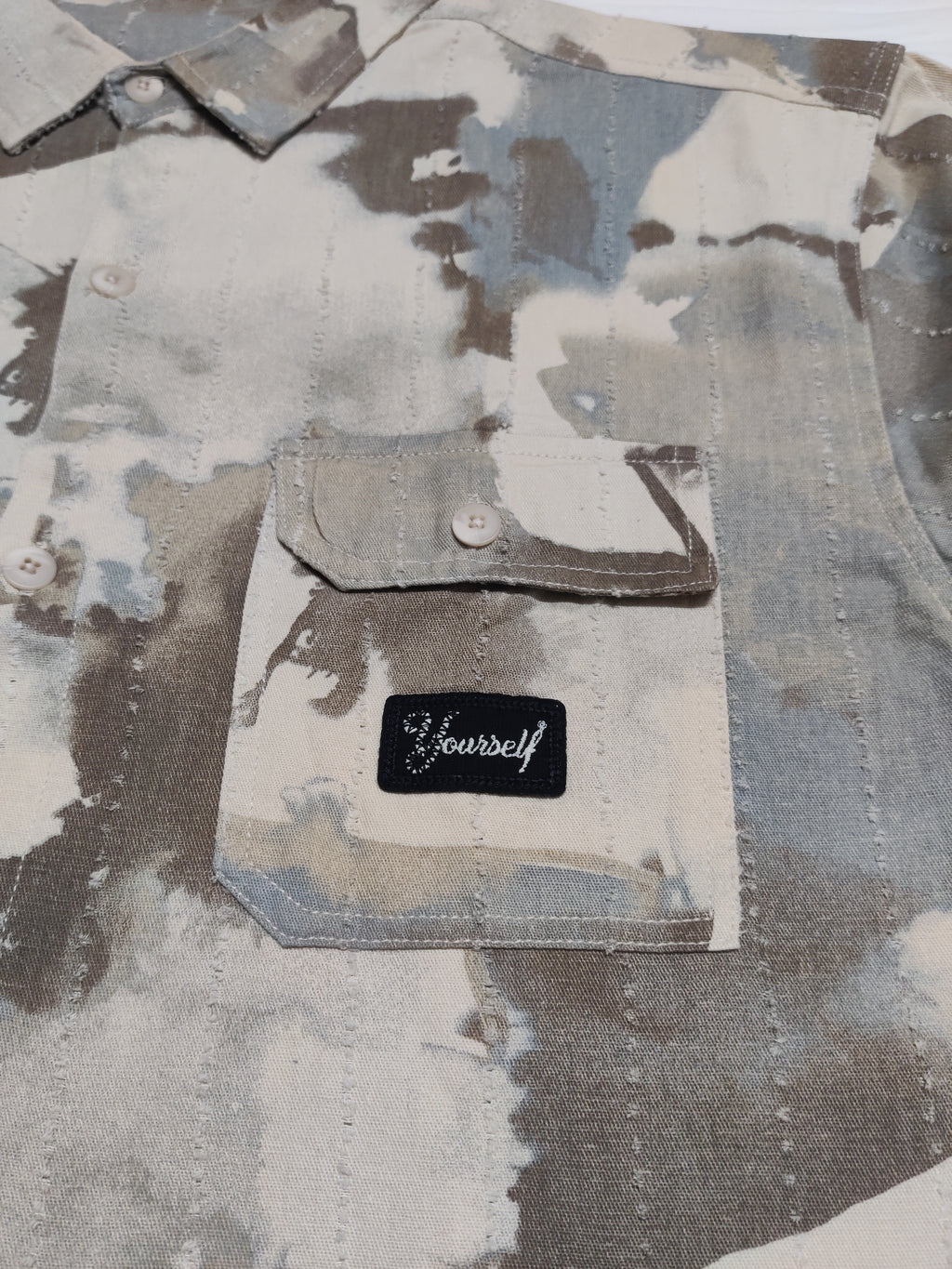 Camouflage-patterned shirt with a patch that says 'Be yourself' on a matching background