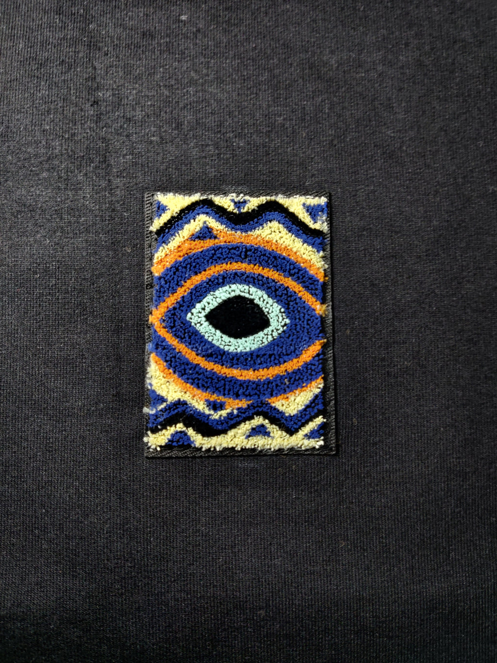 Colorful embroidered patch with eye design on a black background