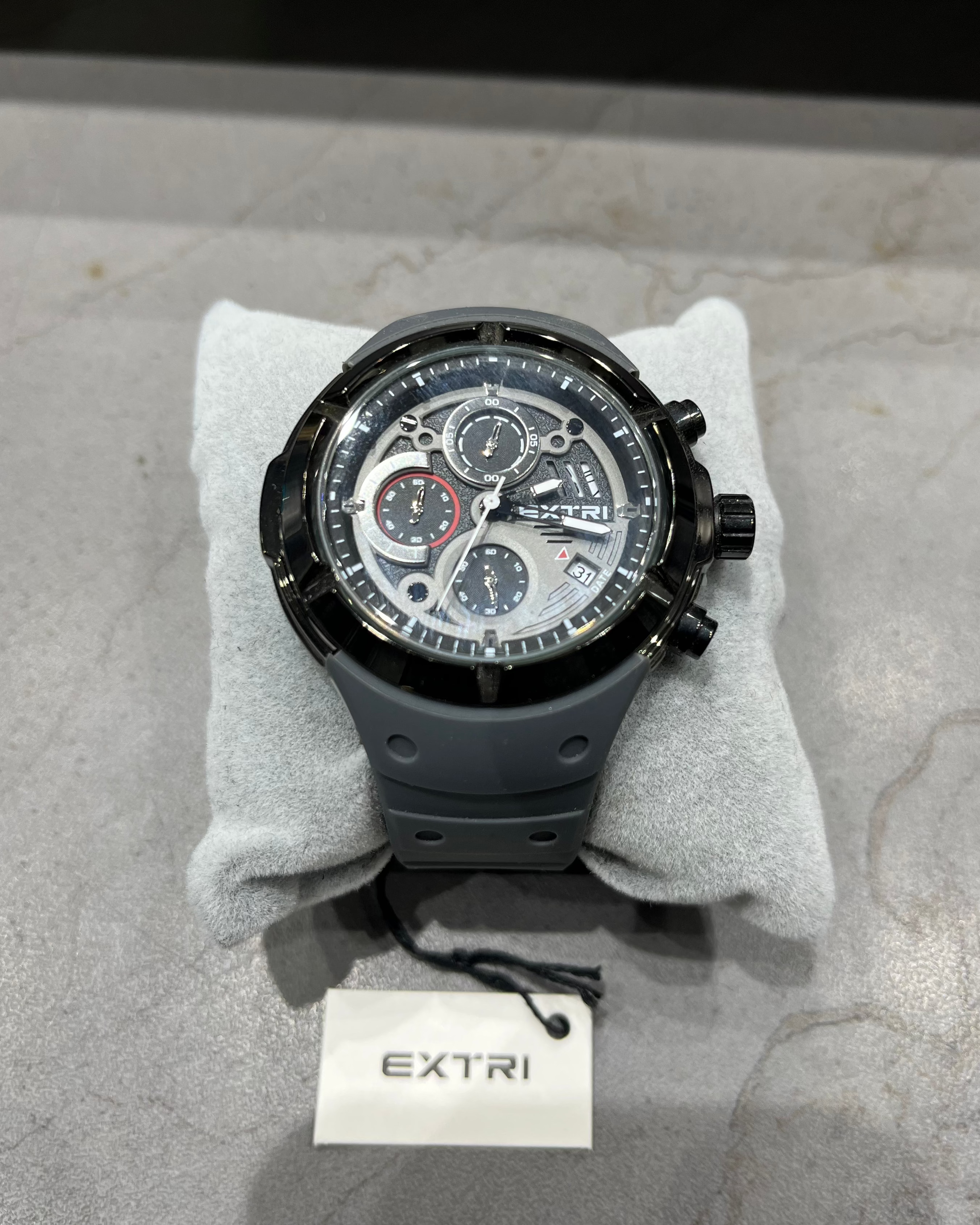Black wristwatch on a gray surface with 'EXTRI' branding visible