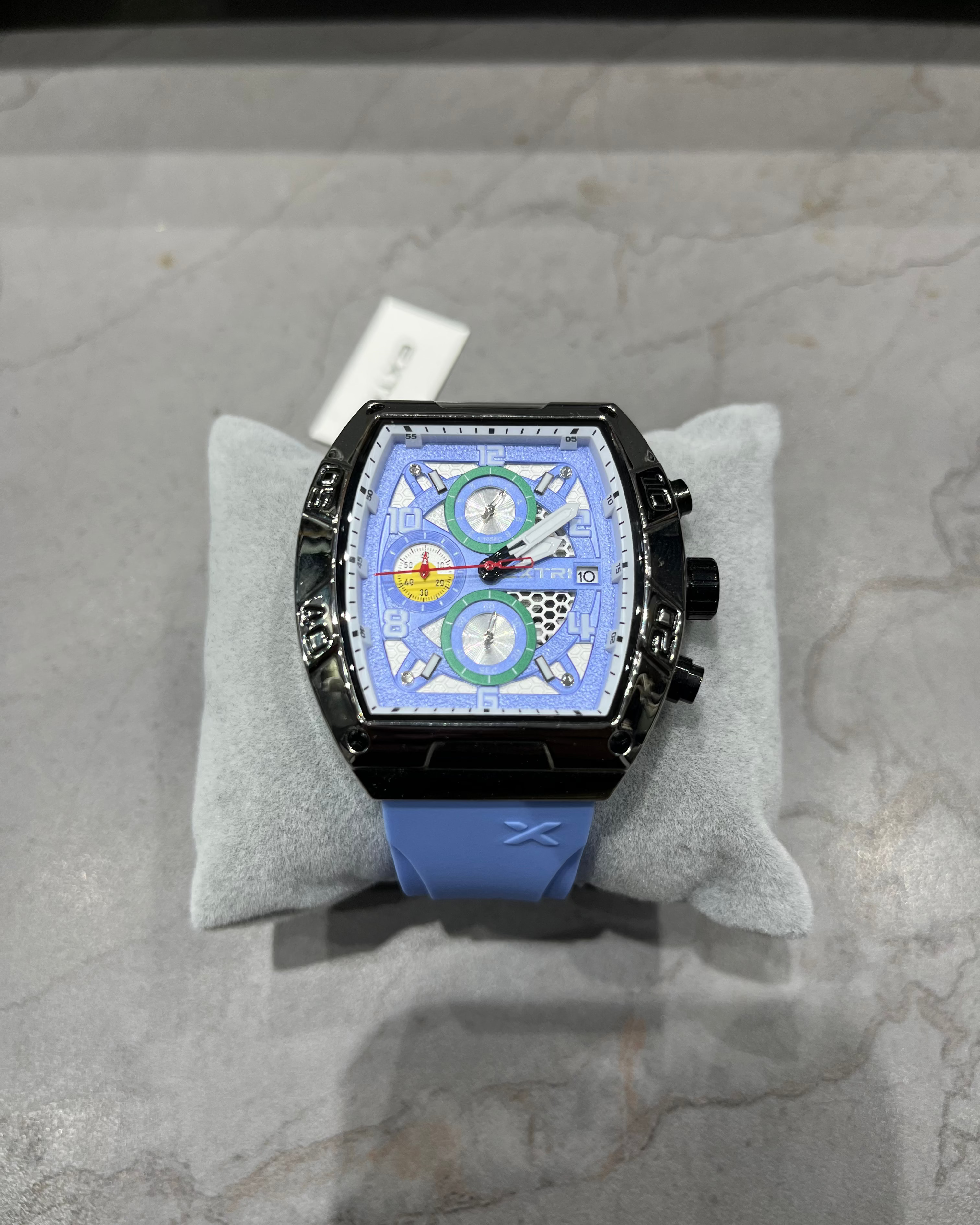Luxury watch with a blue strap on a gray cushion against a marble background