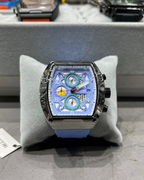 Luxury watch with a blue face on a gray cushion, with a blurred background of other watches.