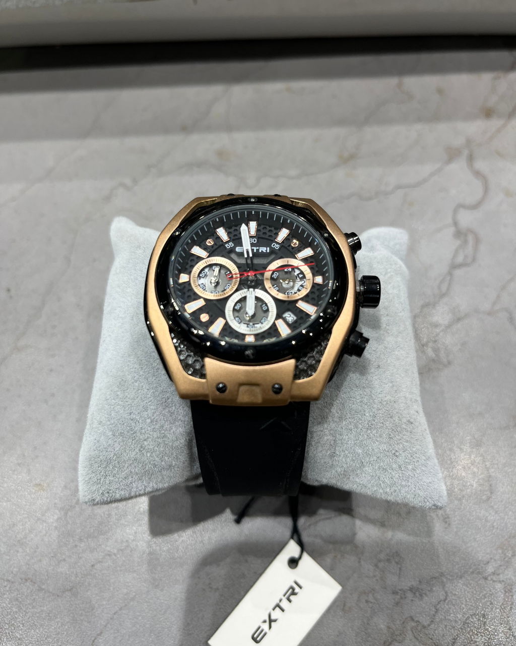 Luxury watch with black face and gold casing on a gray surface, brand 'Extri' visible.