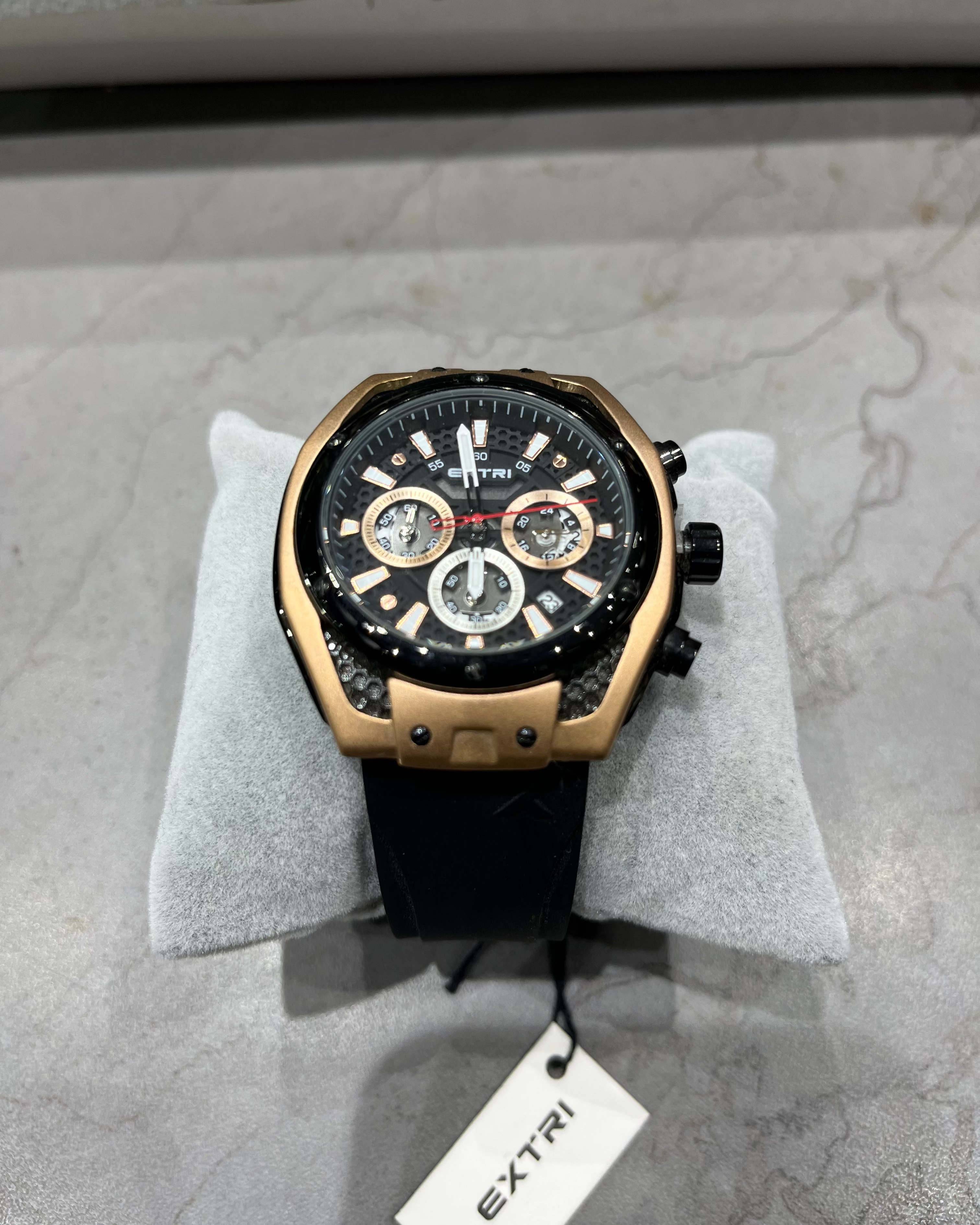Luxury watch with black face and gold casing on a gray surface, brand 'Extri' visible.