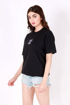 Woman wearing a black t-shirt with a small evil eye patch and light blue denim shorts on a white background