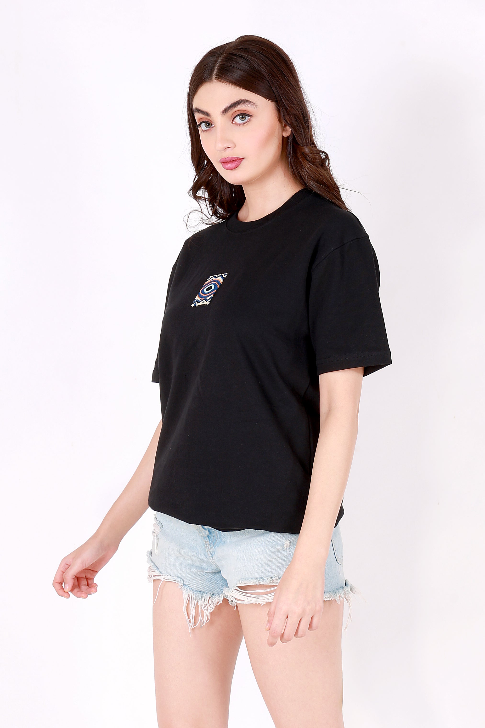 Woman wearing a black t-shirt with a small evil eye patch and light blue denim shorts on a white background