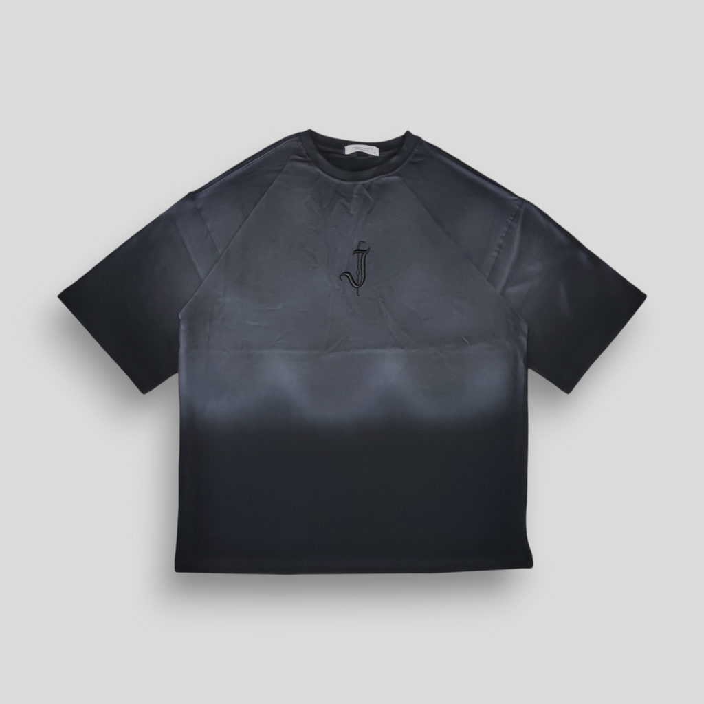 A black oversized T-shirt with a spray-painted front and back gradient and a 3D embroidered 'J' logo in the center.