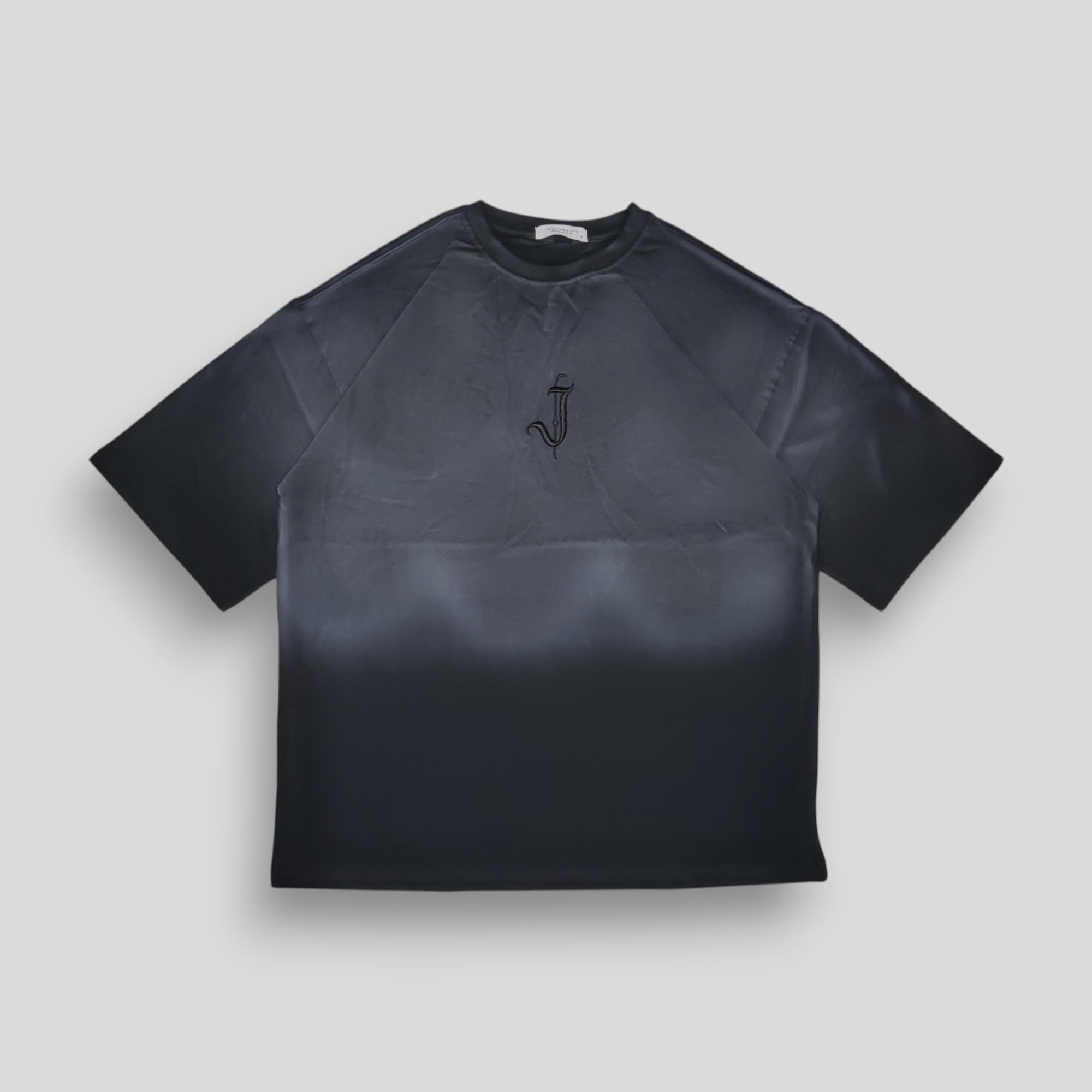 A black oversized T-shirt with a spray-painted front and back gradient and a 3D embroidered 'J' logo in the center.