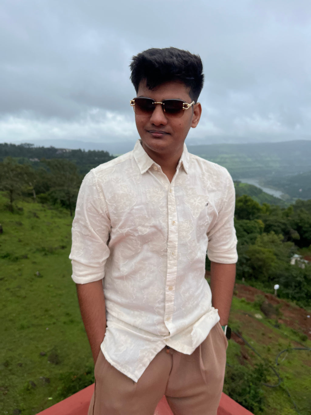 Person wearing sunglasses and a beige linen shirt with a scenic background in mahabaleshwar