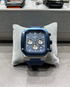 Blue and silver watch on a gray cushion with a blurred background