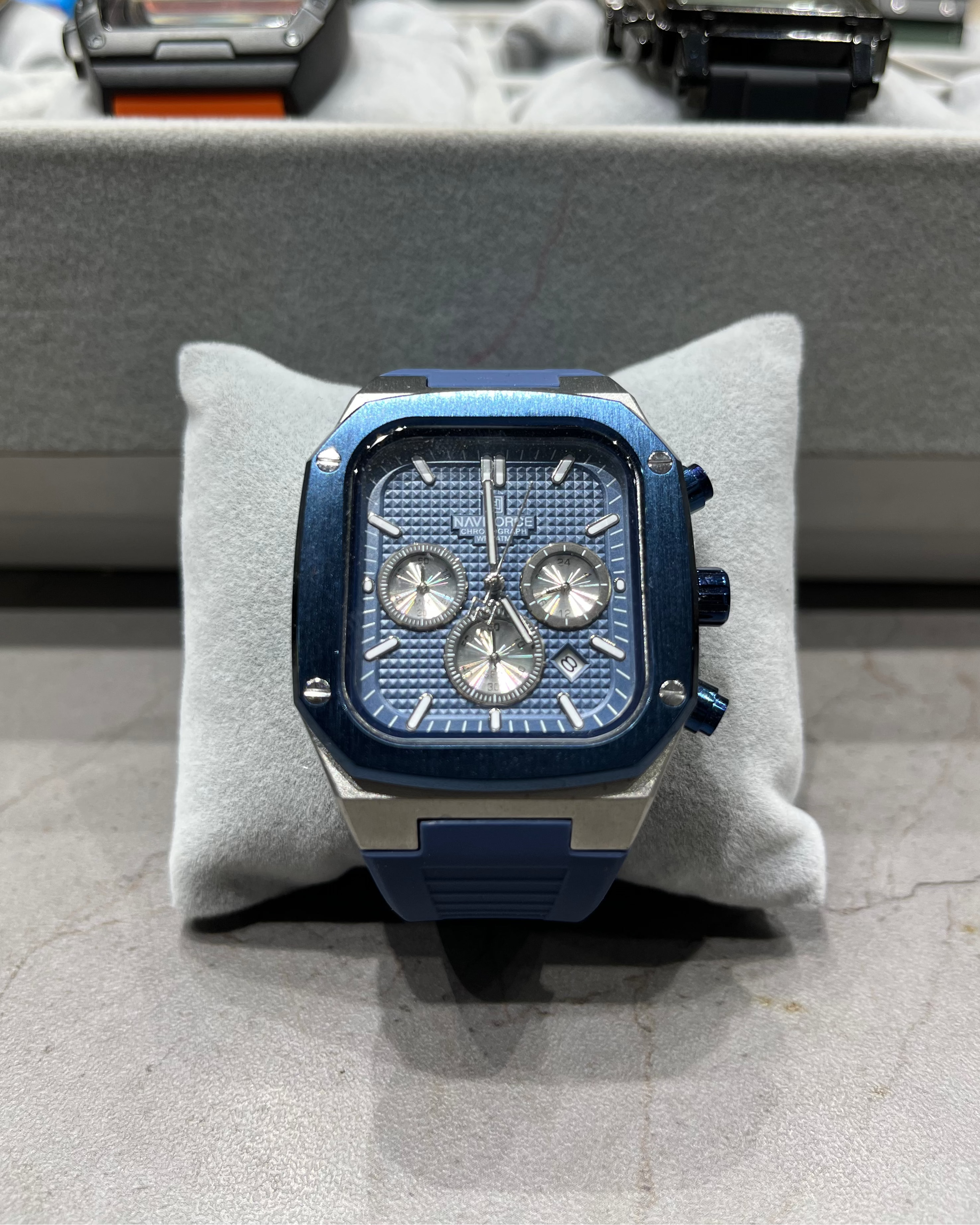 Blue and silver watch on a gray cushion with a blurred background