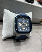 Blue and silver watch on a gray cushion with blurred background