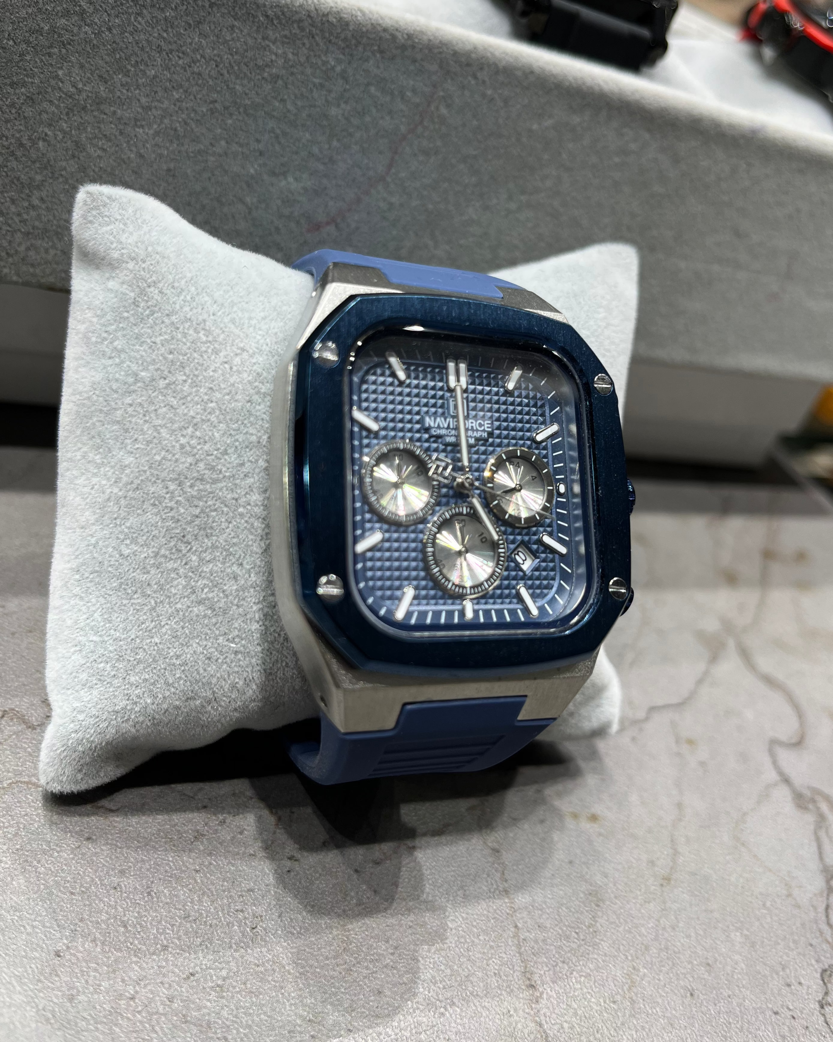 Blue and silver watch on a gray cushion with blurred background