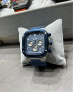 Blue and silver watch on a gray cushion with blurred background