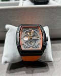 Luxury watch with orange strap on a gray cushion, blurred background
