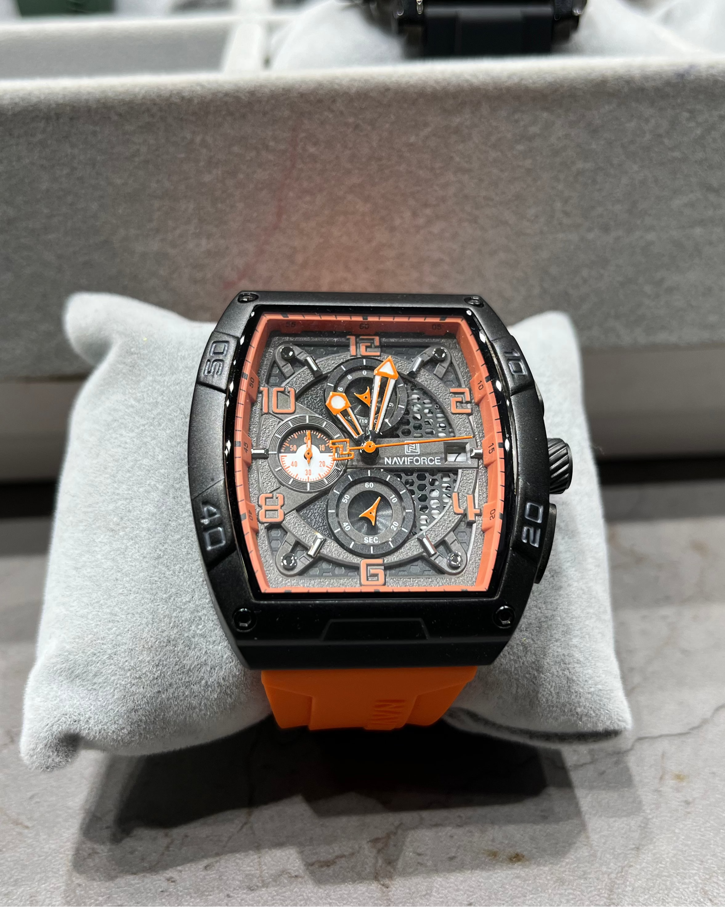 Luxury watch with orange strap on a gray cushion, blurred background