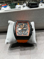 Luxury watch with black and orange design on a gray cushion