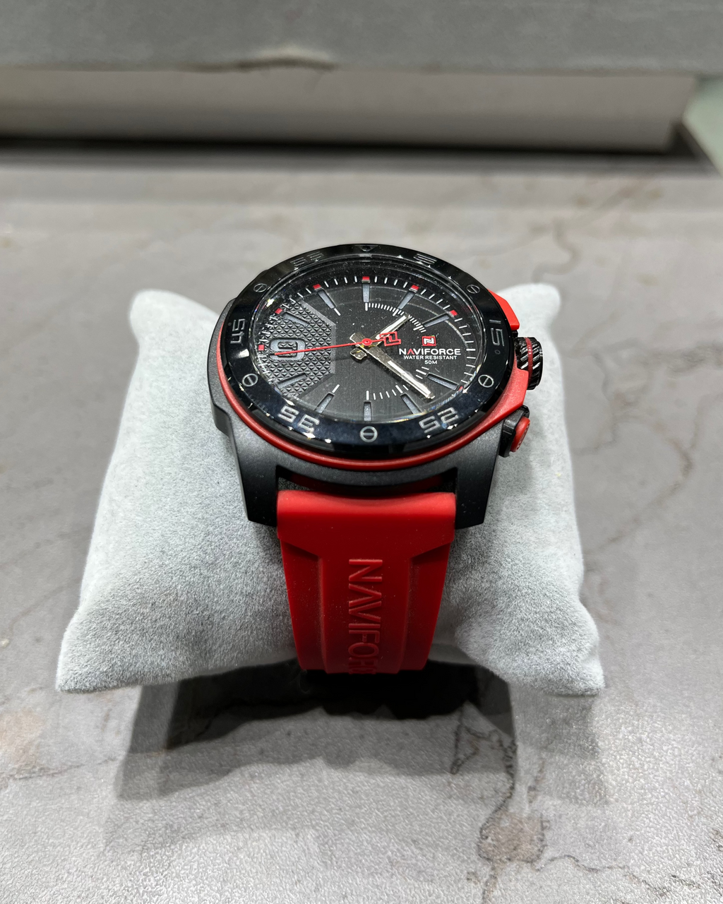 Watch with red strap on a gray cushion against a concrete background