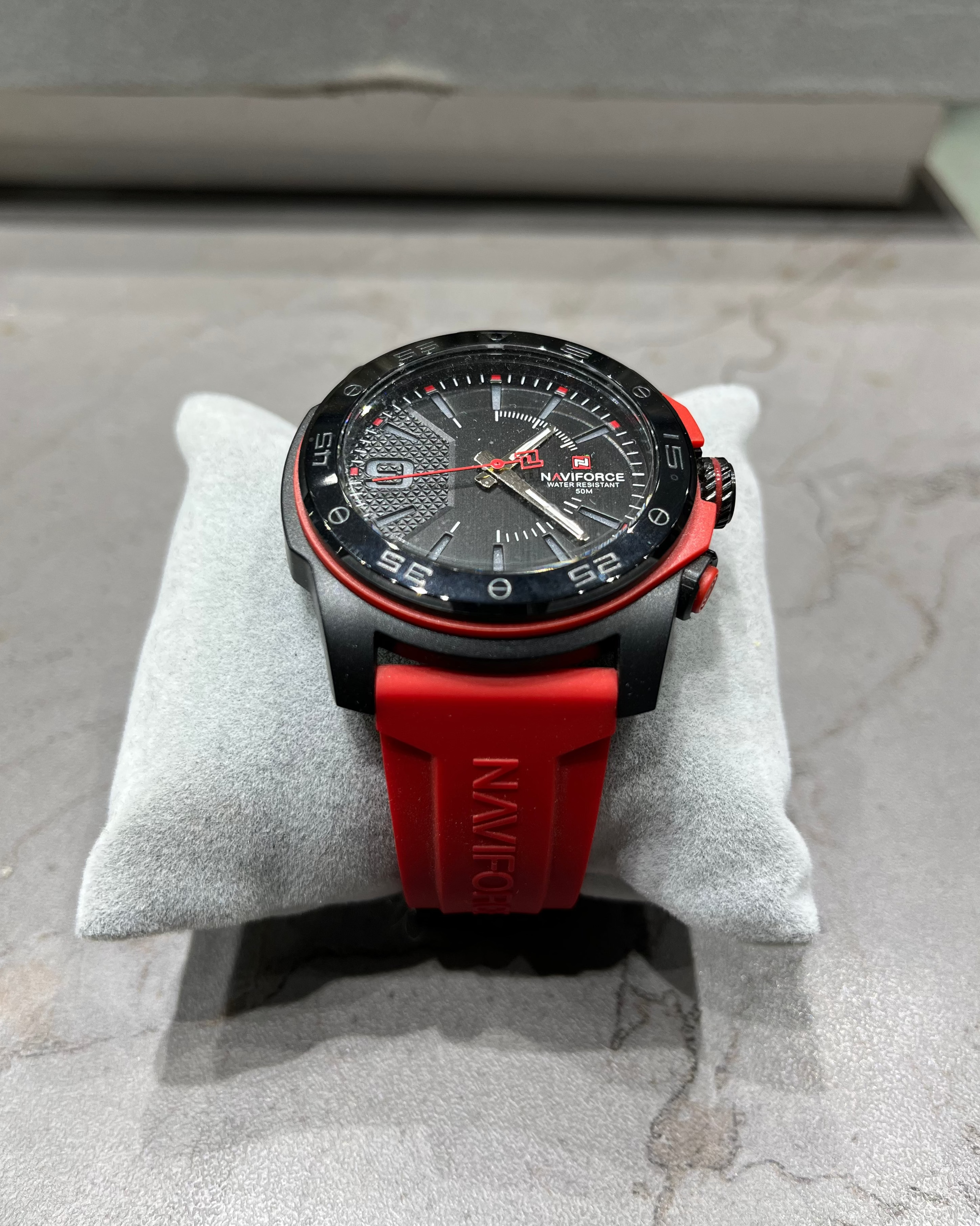 Watch with red strap on a gray cushion against a concrete background