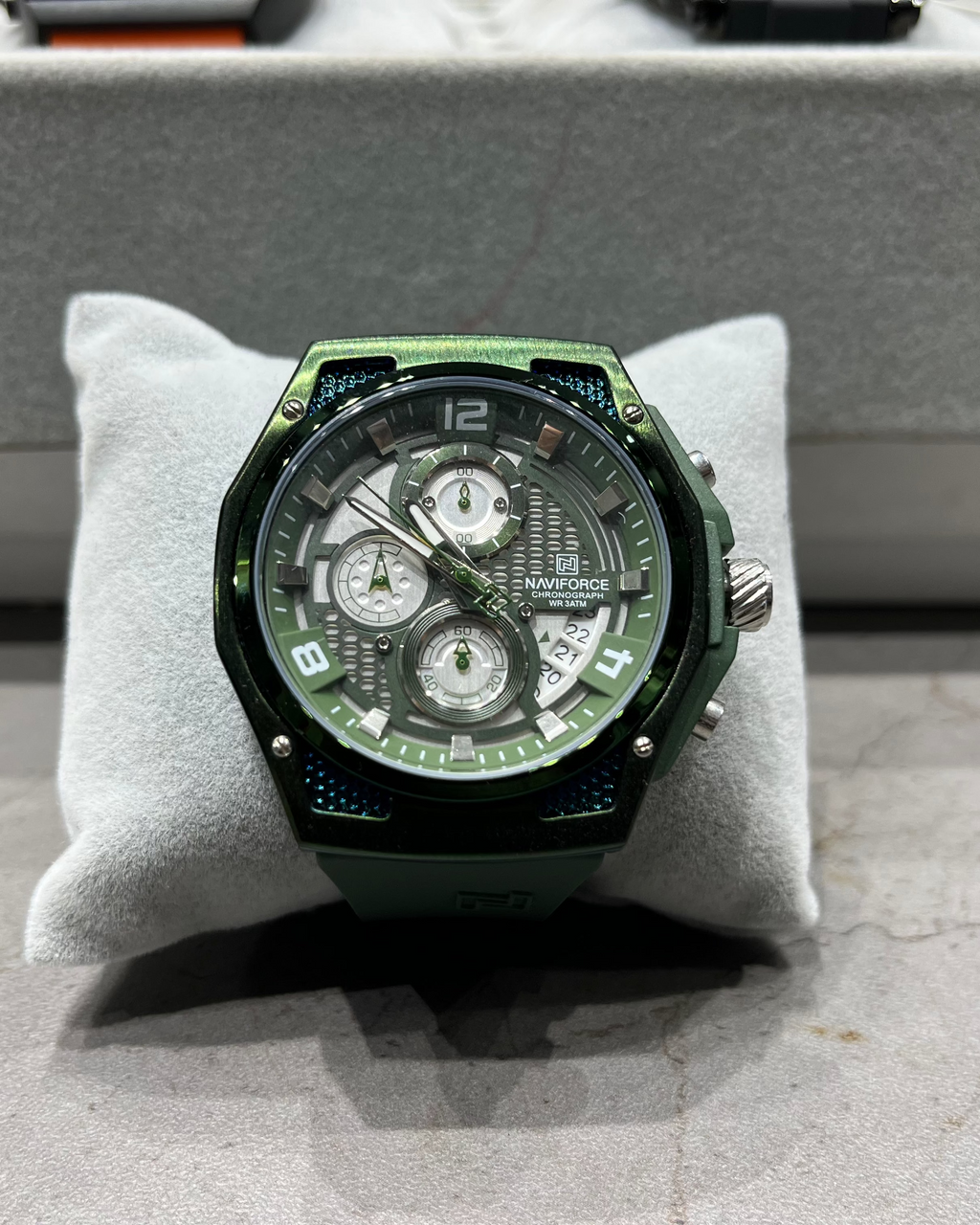 Green wristwatch on a gray cushion with a neutral background