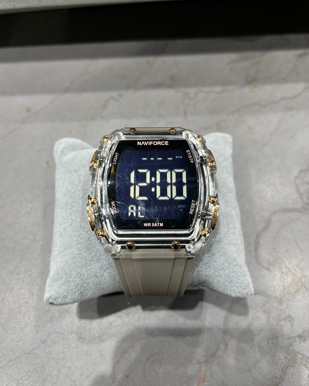 Digital watch with gold accents on a gray cushion against a marble background