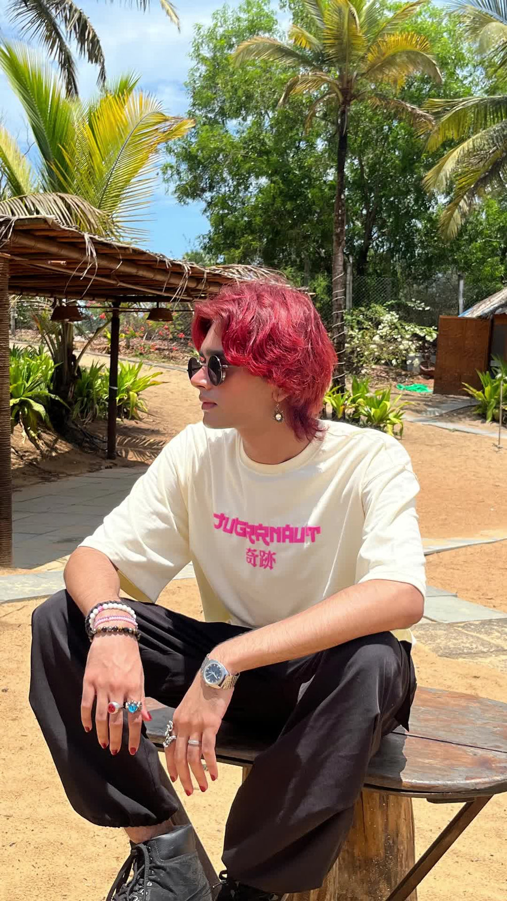 Person with pink hair sitting outdoors in a tropical setting