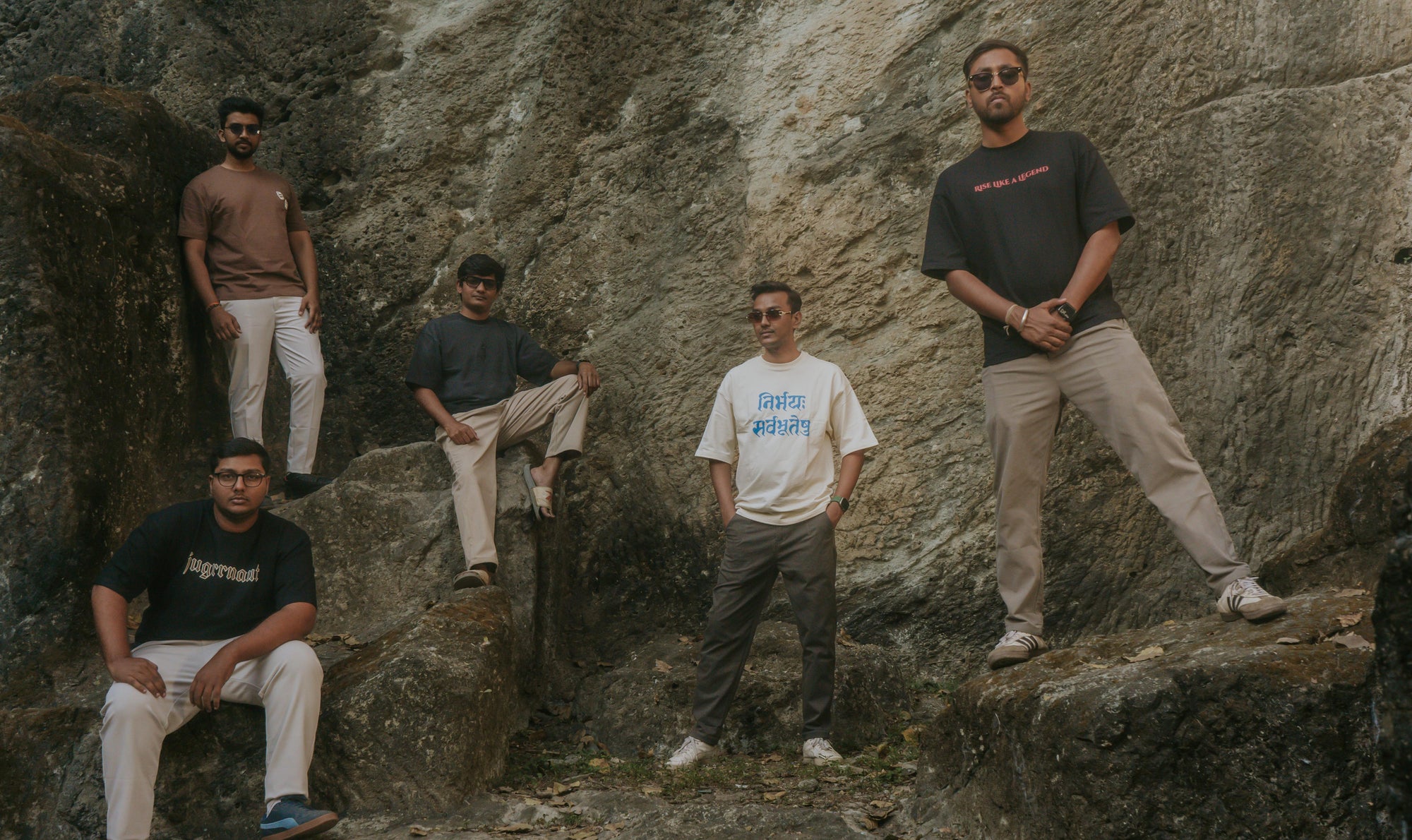 Five men posing on rocky terrain with a natural rock formation background