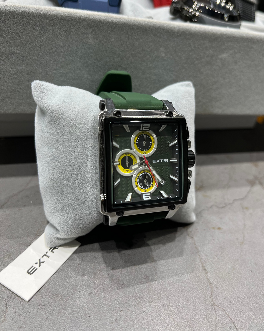 Watch with green strap on a gray cushion, brand 'Extri' visible