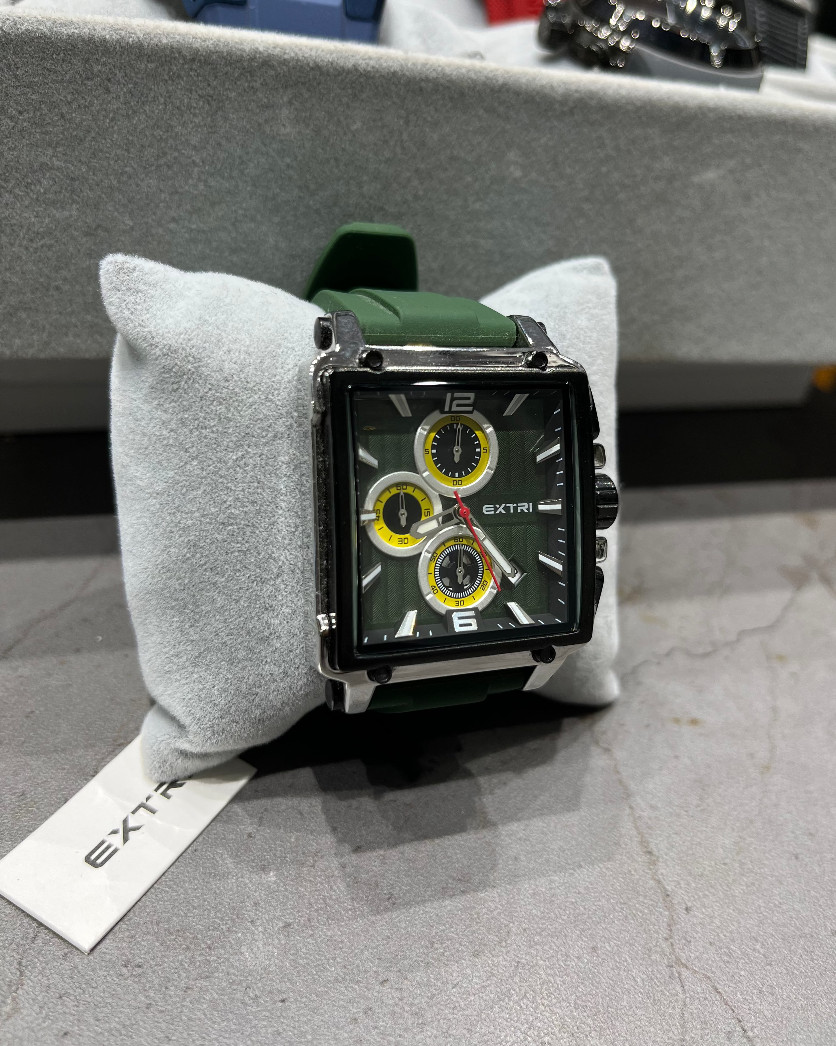 Watch with green strap on a gray cushion, brand 'Extri' visible