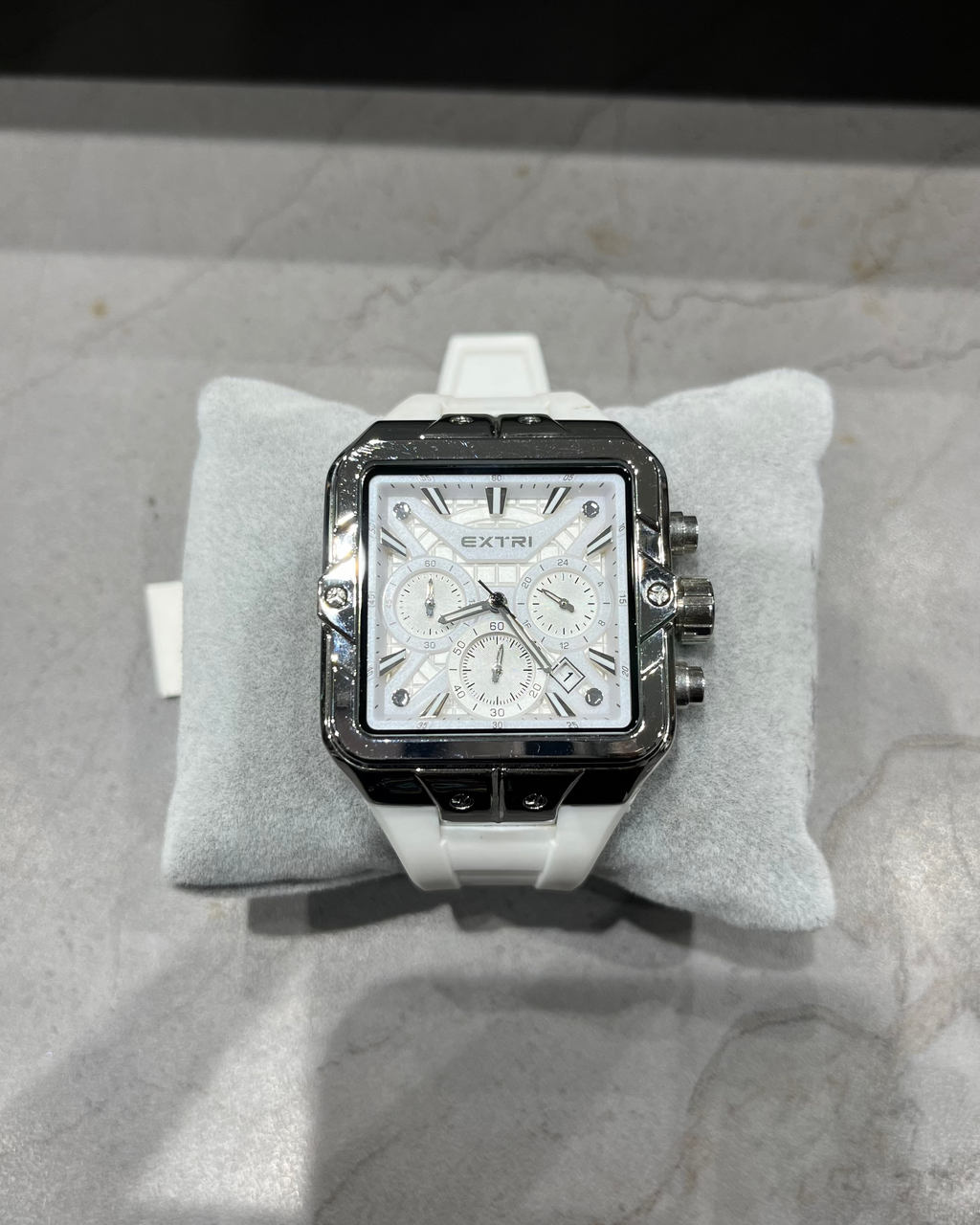 Watch with a white strap on a gray cushion, brand 'Extri' visible