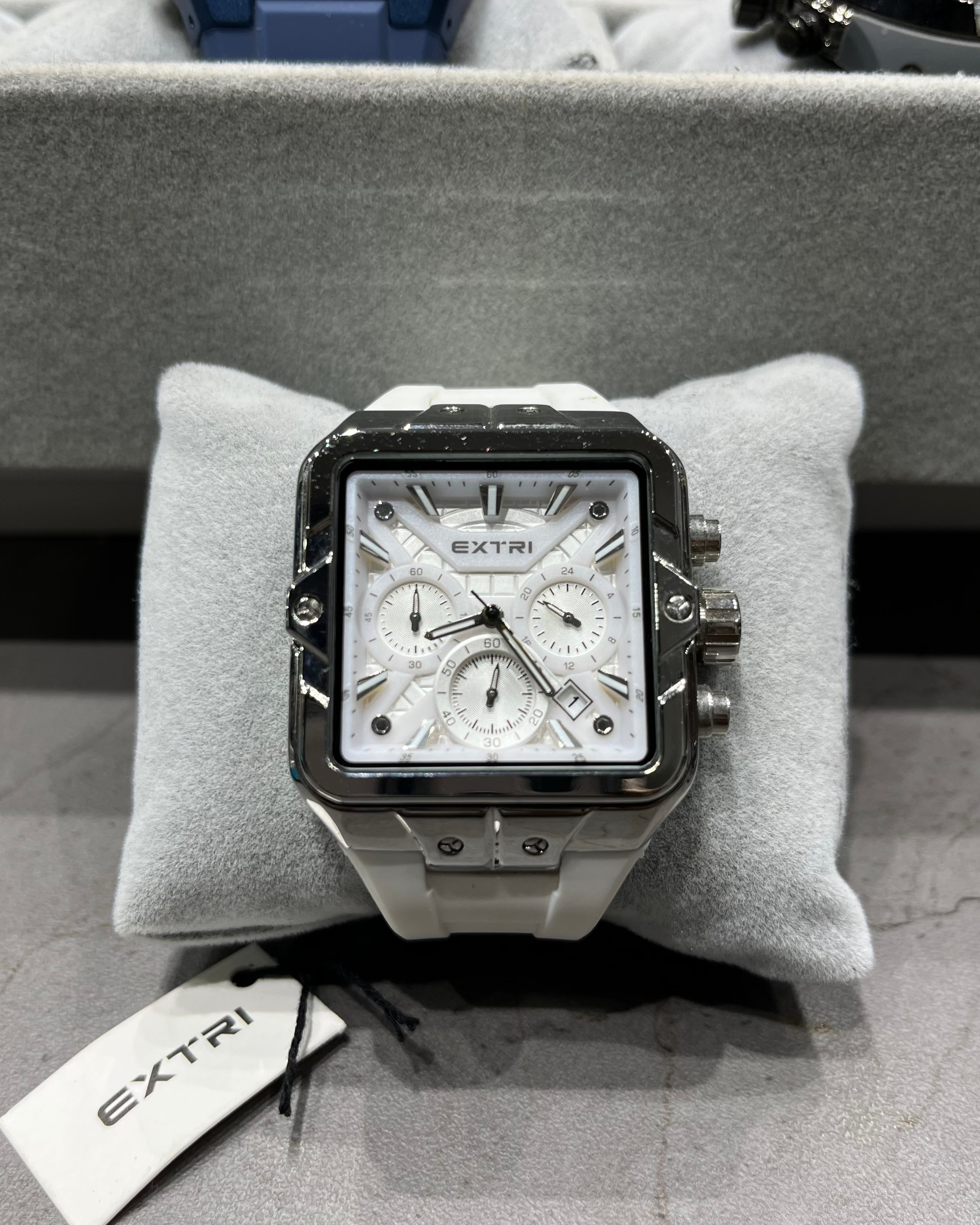 Luxury watch with 'Extri' branding on a gray cushion with a blurred background.