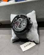 Luxury watch with visible brand name on a gray cushion, with a blurred background of other watches.