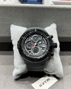 Black Extri watch on a gray cushion with a branded box in the background