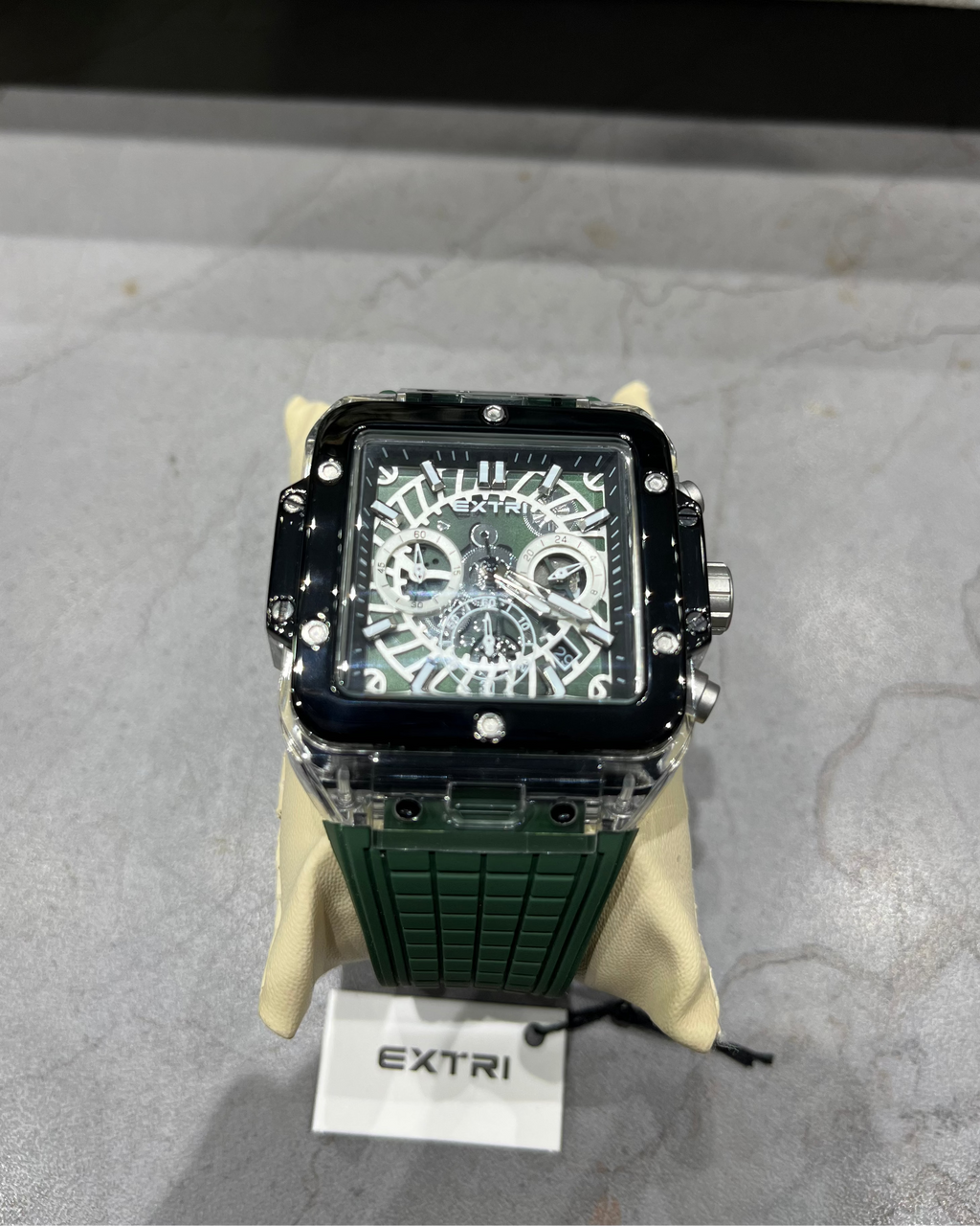 Green watch with black face on a gray surface, branded 'Extri'.