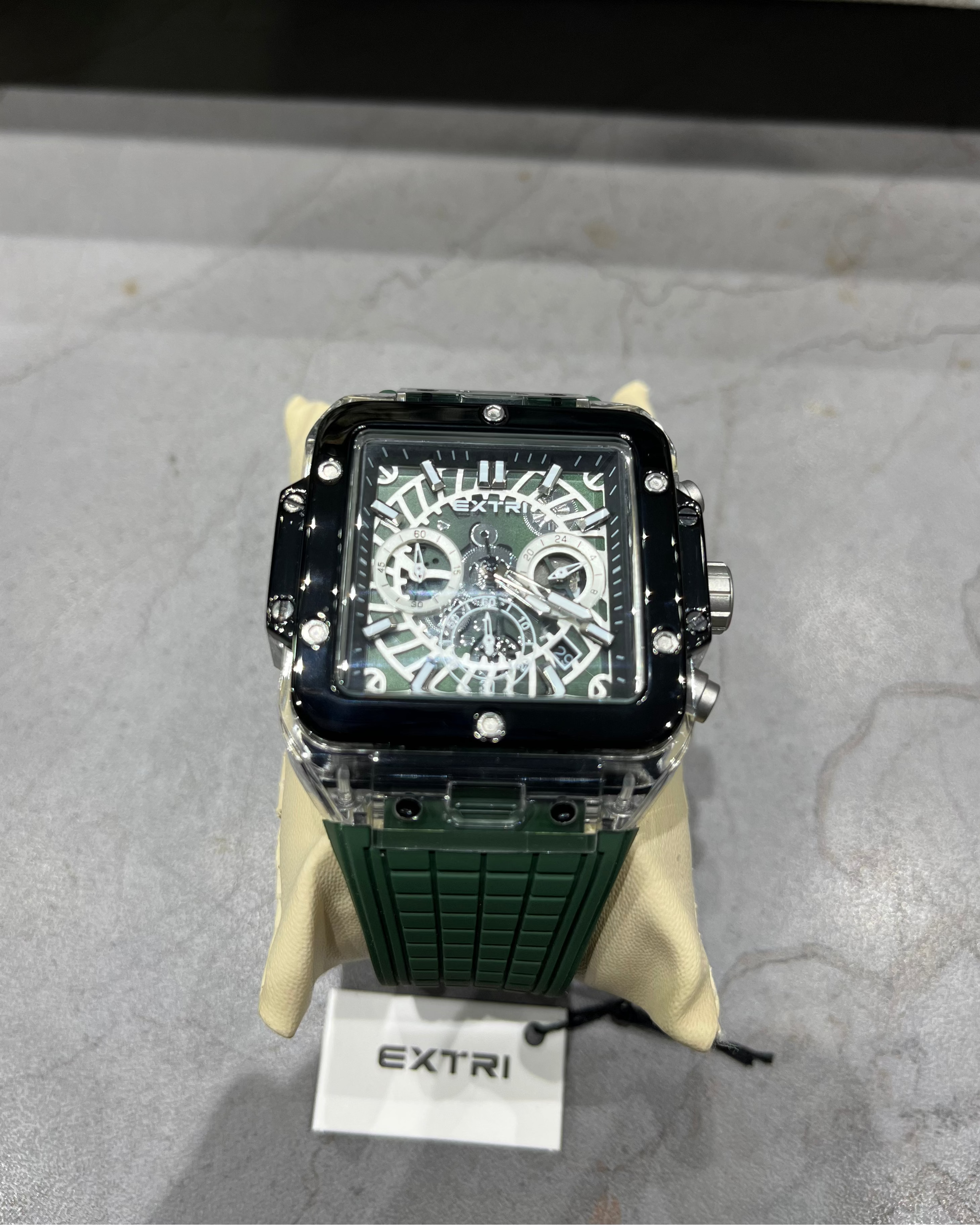 Green watch with black face on a gray surface, branded 'Extri'.