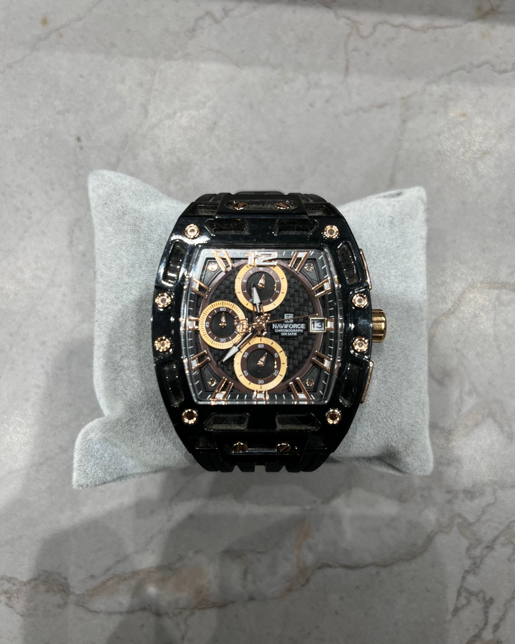 Luxury watch with black and gold design on a gray cushion against a marble background