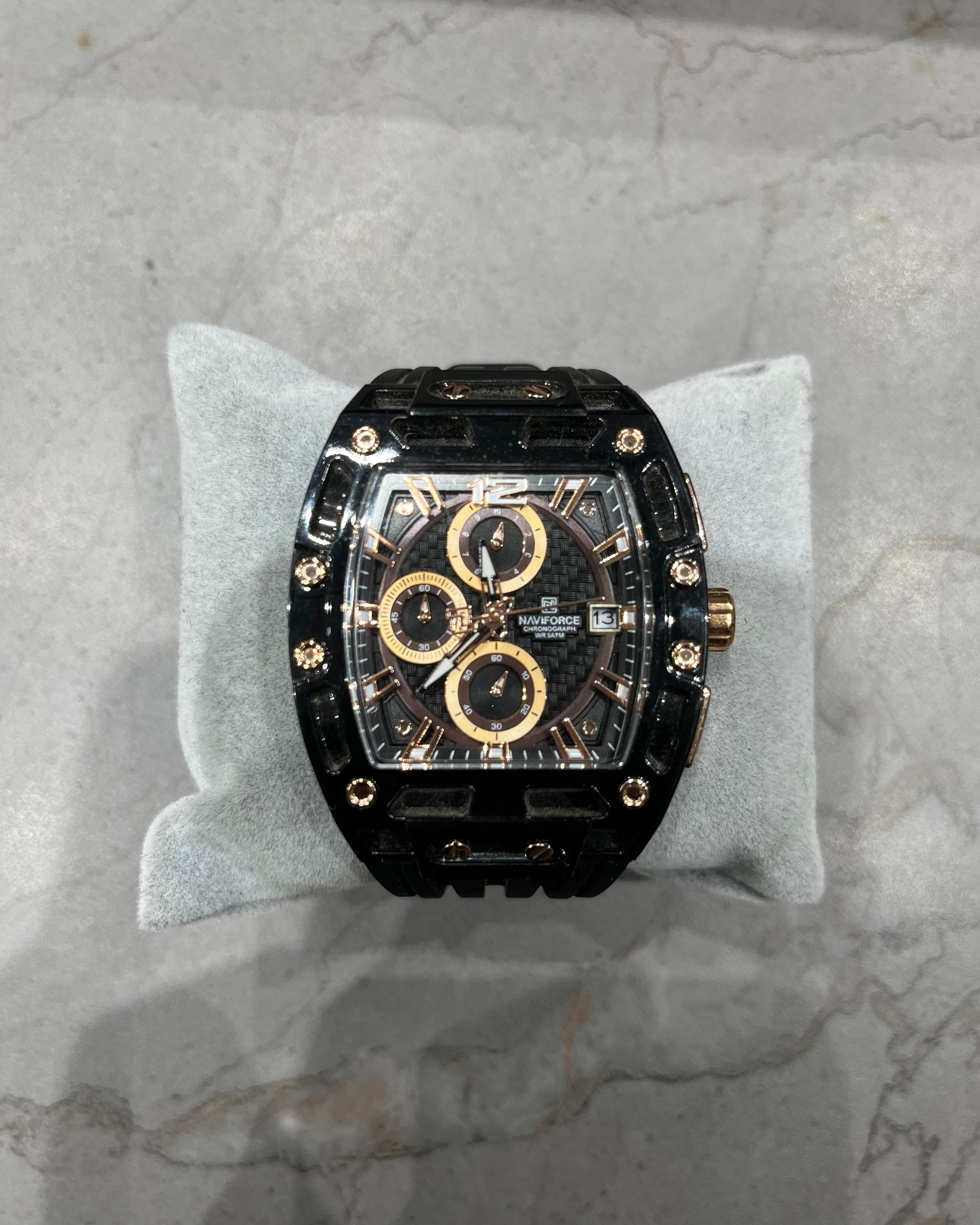 Luxury watch with black and gold design on a gray cushion against a marble background