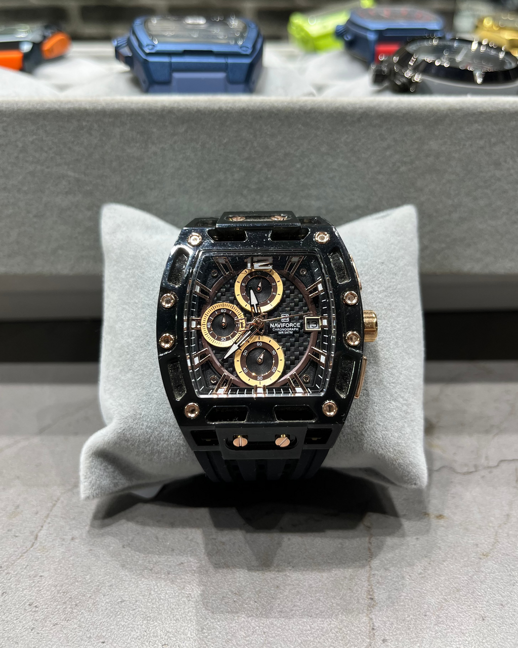 Luxury watch with black and gold design on a gray stand, blurred background