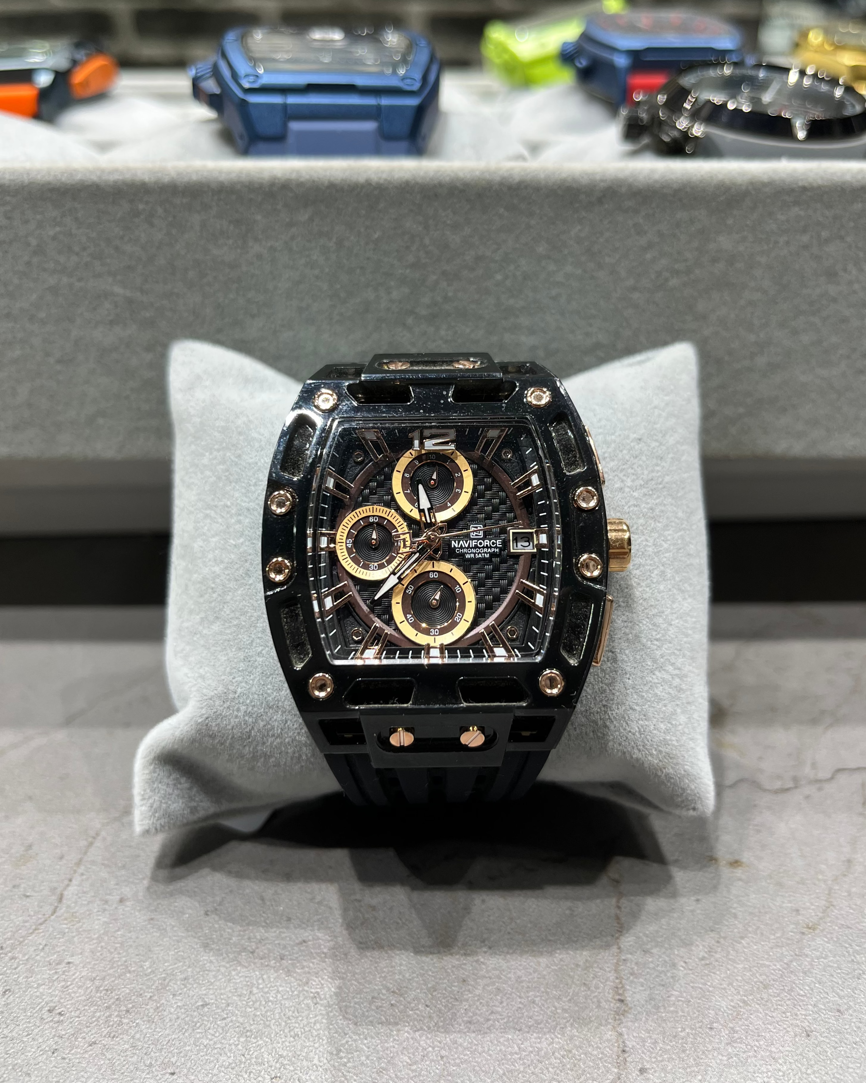Luxury watch with black and gold design on a gray stand, blurred background