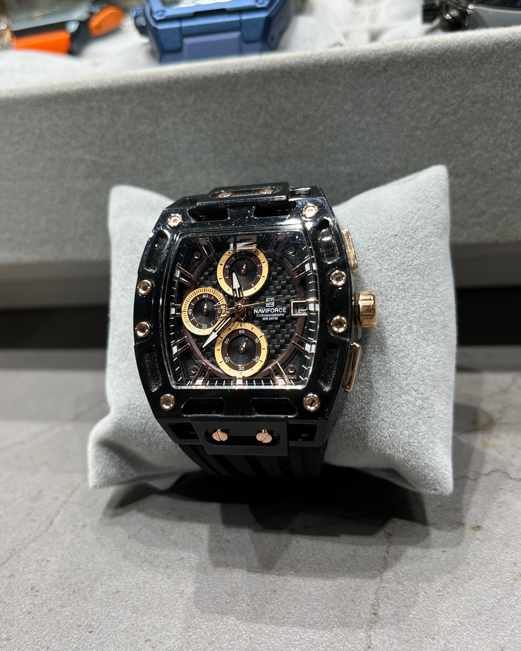 Luxury watch with black and gold design on a gray cushion, blurred background