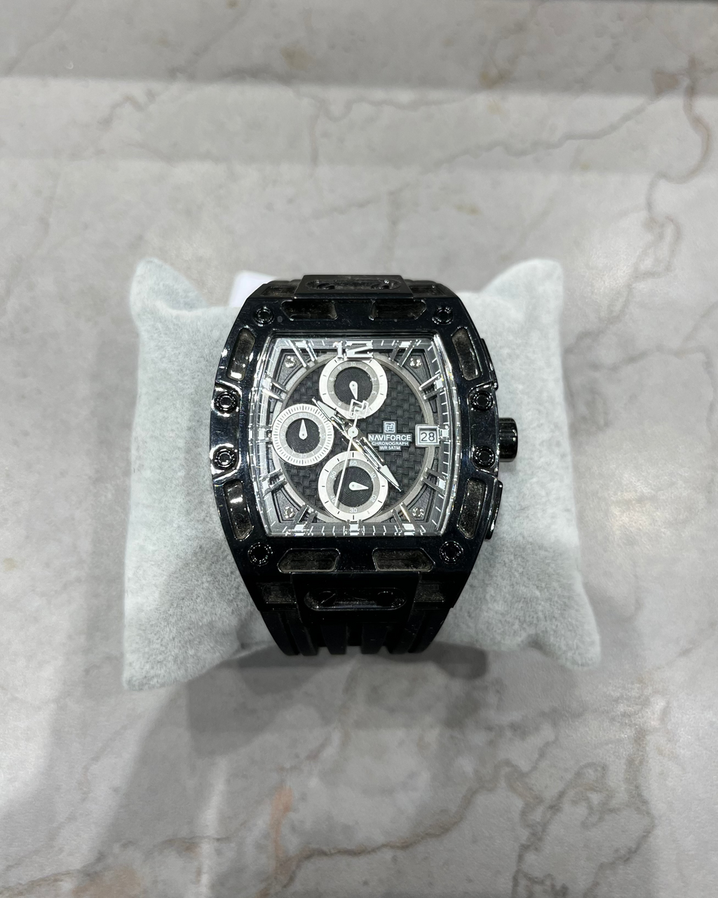 Black luxury watch on a white cushion with a marble background
