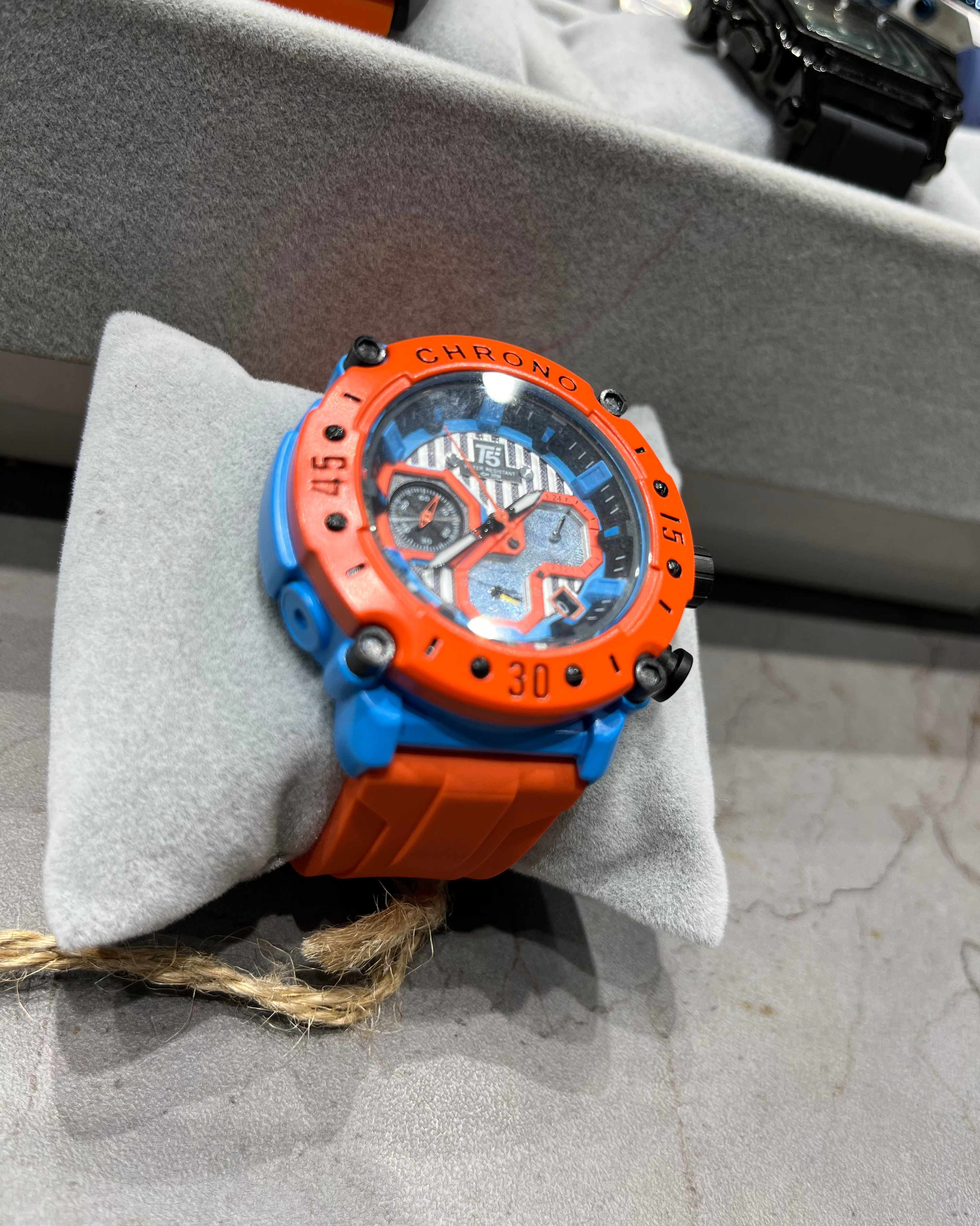 Orange and blue watch on a gray surface with blurred background