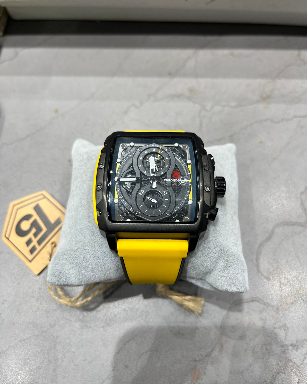 Watch with yellow strap on a gray surface, brand tag visible