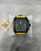 Black and yellow watch on a gray marble surface with a brand tag.