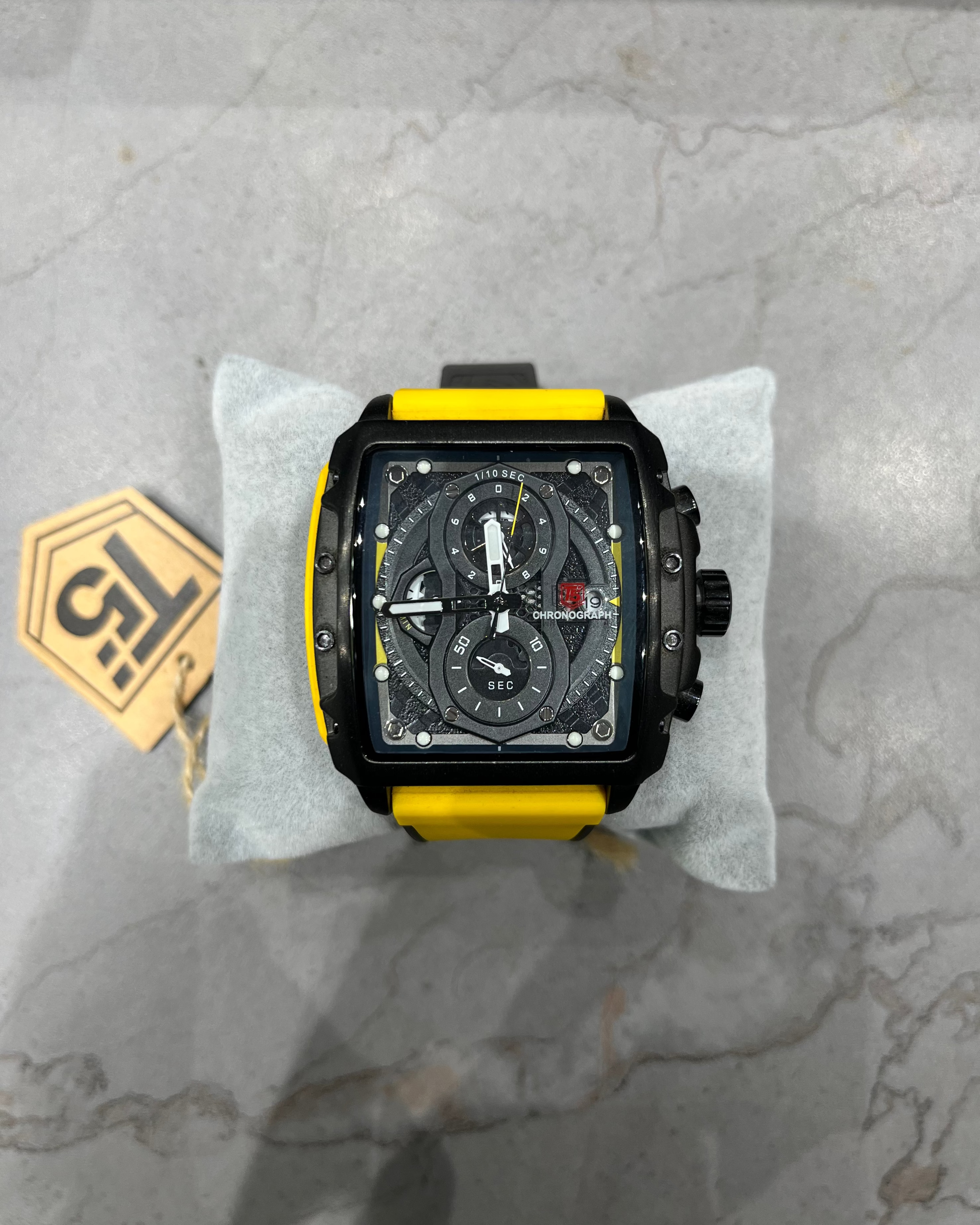 Black and yellow watch on a gray marble surface with a brand tag.