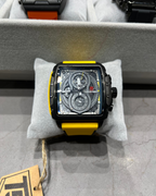 Watch with a yellow strap on a gray surface, with another watch in the background.