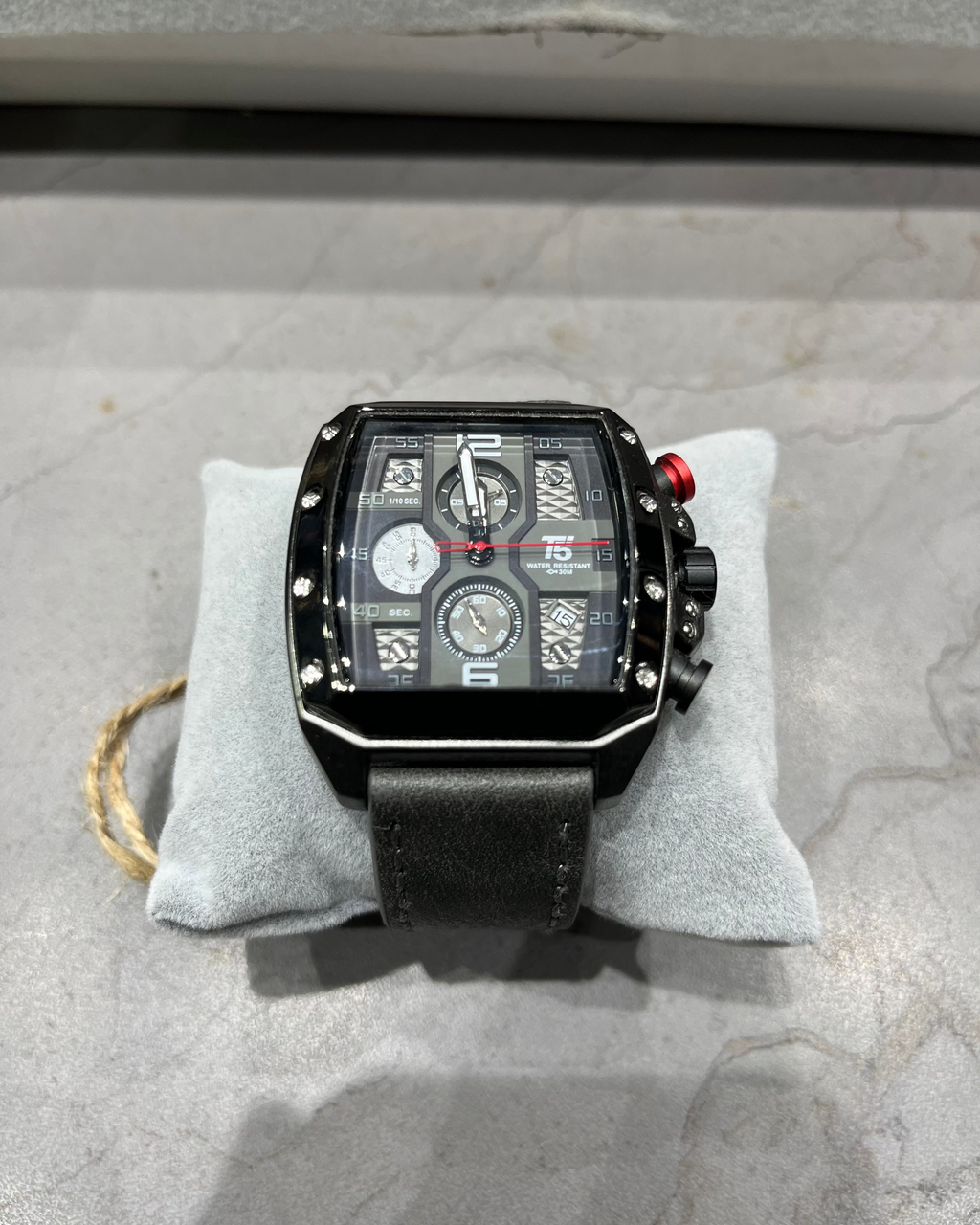 Black wristwatch with detailed face on a gray cushion, on a textured surface