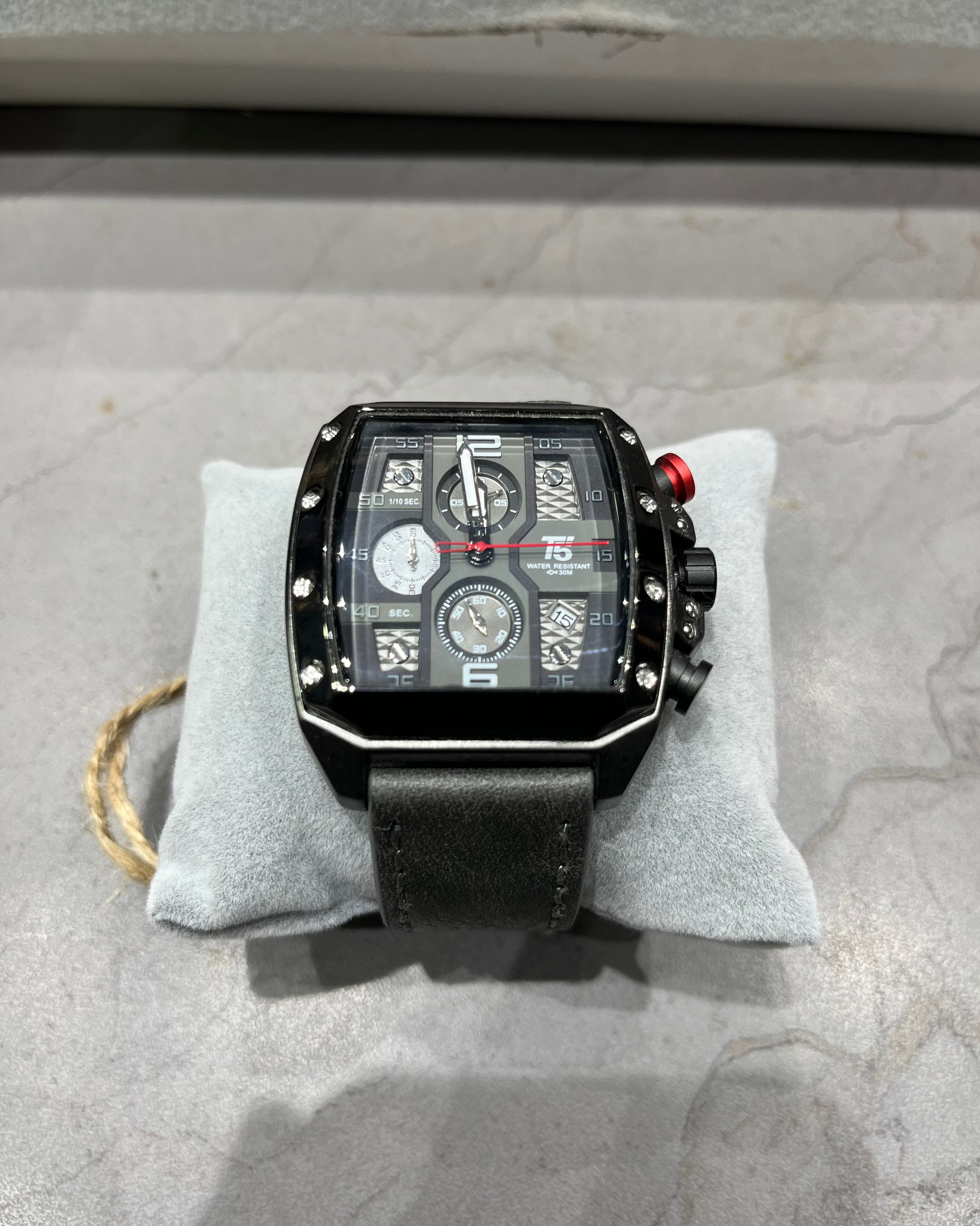 Black wristwatch with detailed face on a gray cushion, on a textured surface