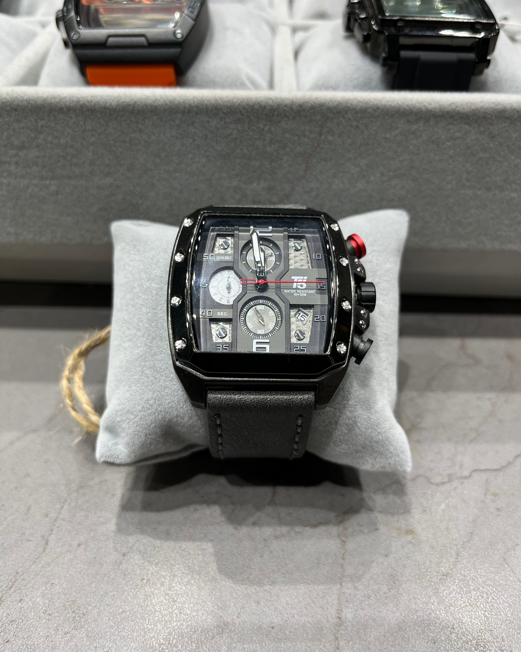 Black wristwatch on a gray cushion with other watches in the background