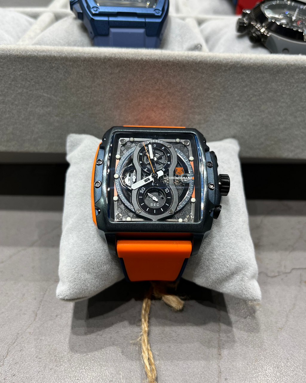 Watch with orange strap on a gray surface, surrounded by other watches.